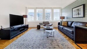 A modern living room with a large flat-screen TV, a dark leather sofa, a coffee table, and a patterned rug. - Modern One Bedroom Apartment in Boston's Back Bay (Boston)