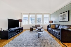 Un salon moderne doté d’un grand téléviseur à écran plat, d’un canapé en cuir foncé, d’une table basse et d’un tapis à motifs.