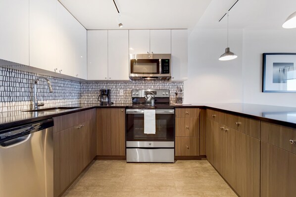 A modern kitchen with stainless steel appliances, wooden cabinets, and a tiled backsplash.