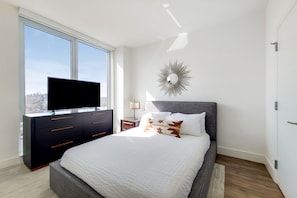 A bedroom with a bed, a TV on a dresser, a mirror on the wall, and a window with a view. - Stylish One Bedroom in White Plains - Near transit (White Plains)