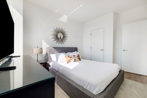 Un dormitorio moderno con cama, mesita de noche, lámpara y un espejo decorativo.