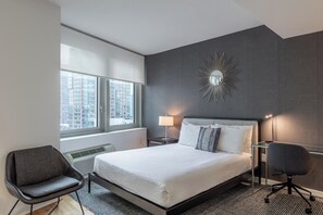 Een moderne hotelkamer met een groot bed, een bureau, een stoel, een raam met uitzicht over de stad en een decoratieve spiegel aan de muur.