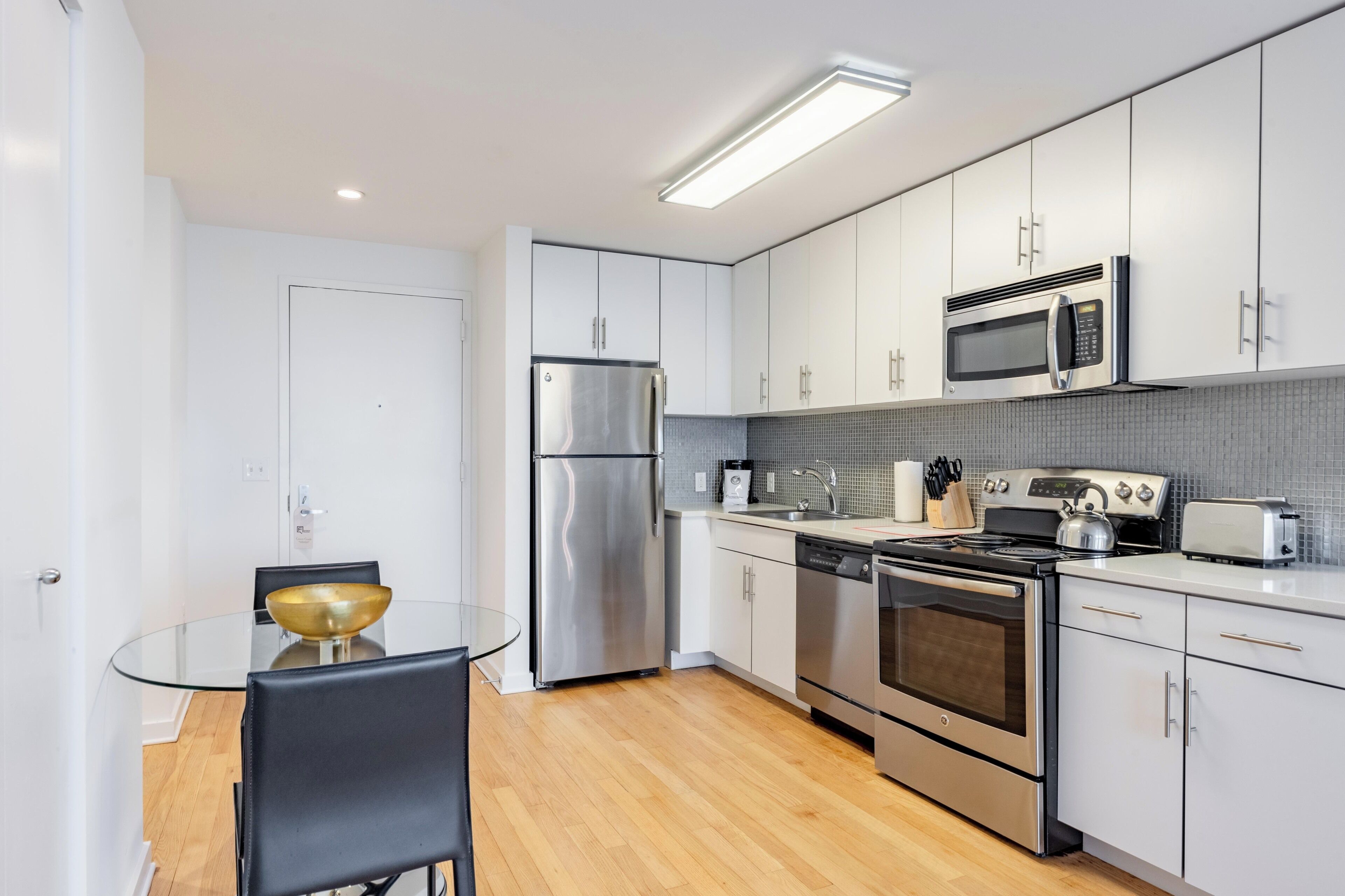 A modern kitchen with stainless steel appliances, white cabinets, and a glass dining table.