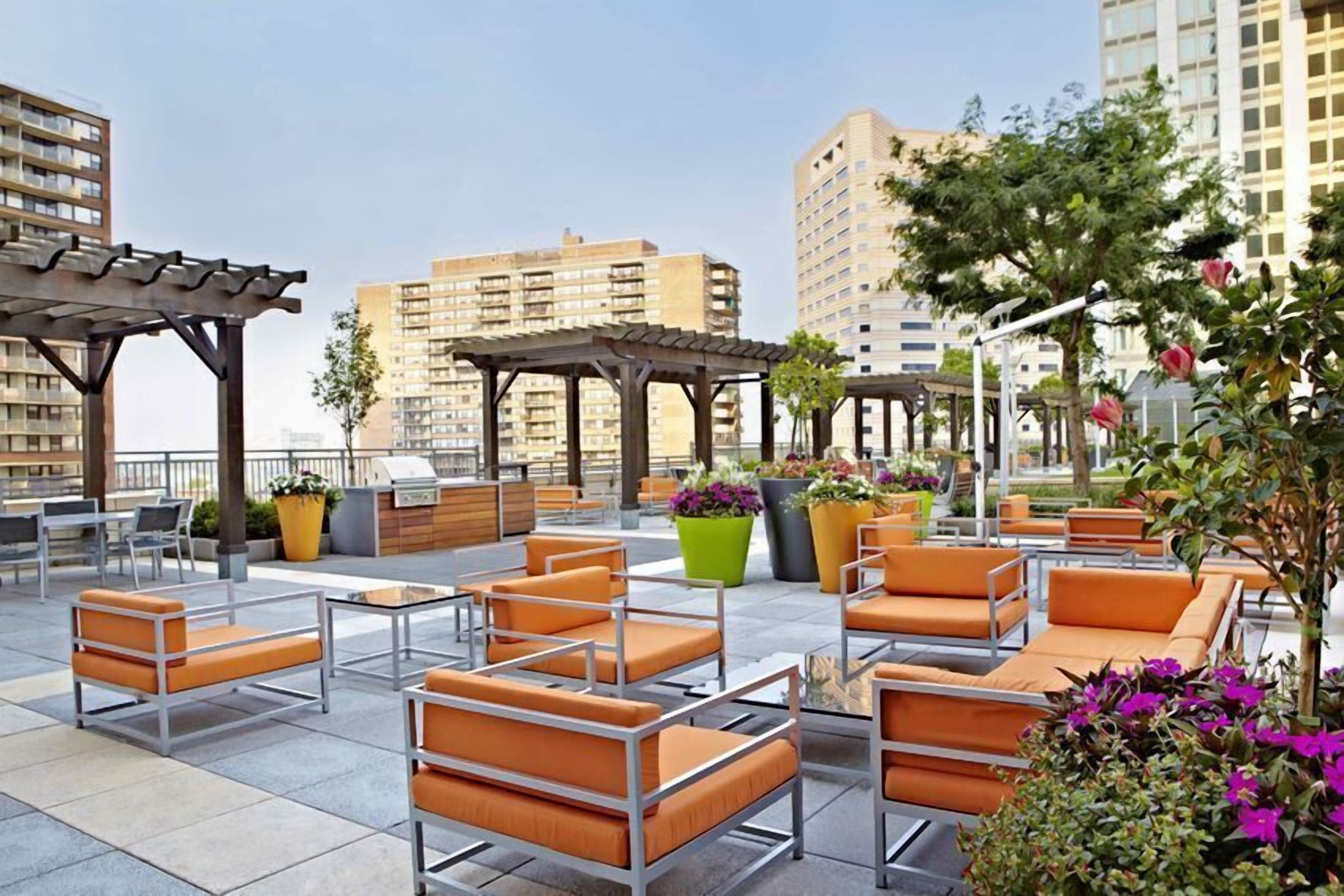 Un espace extérieur aménagé avec plusieurs tables et chaises, entouré de jardinières fleuries.