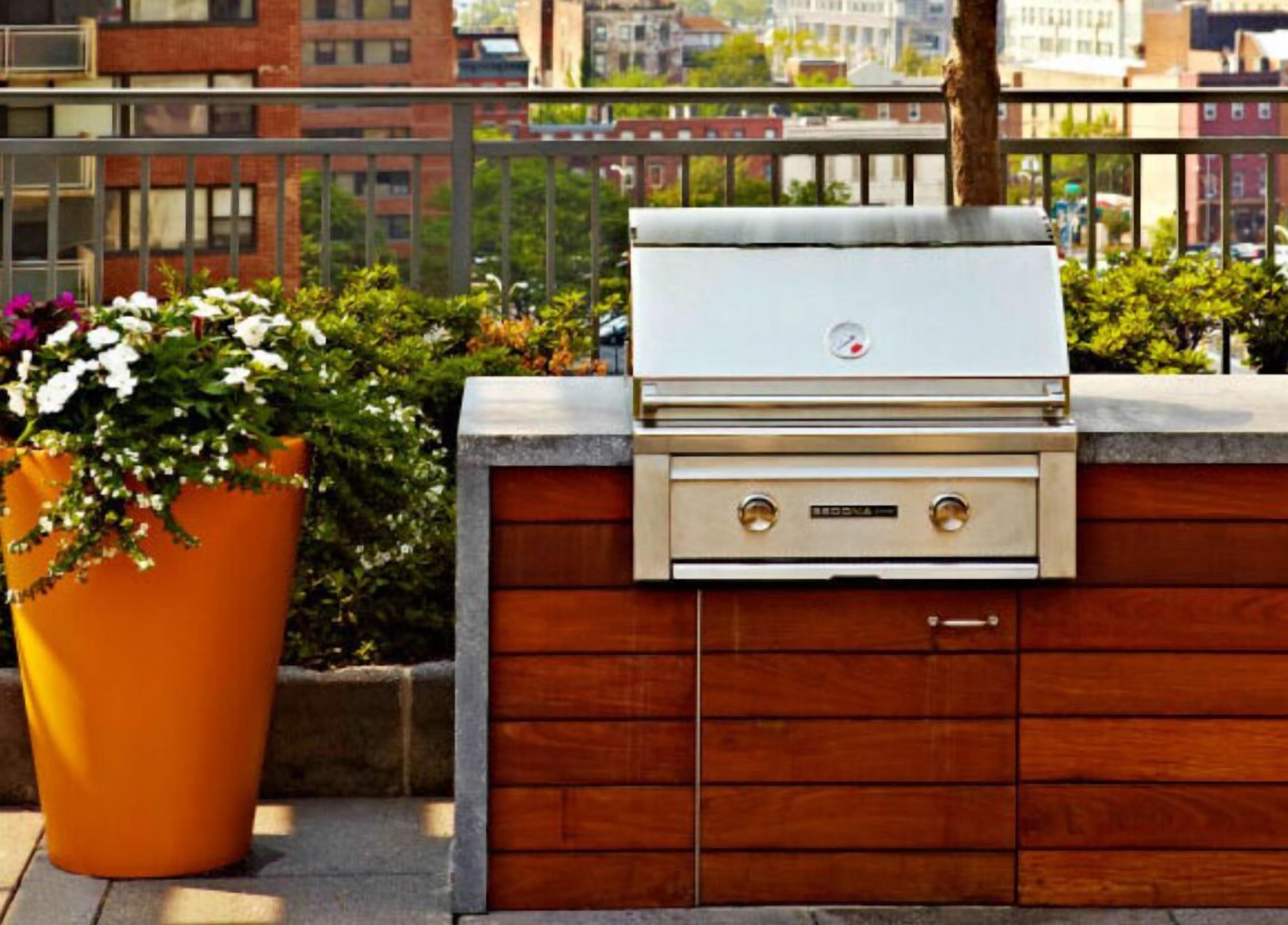 An outdoor grill with a wooden cabinet and a potted plant beside it.