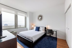 A modern hotel room with a large bed, a desk, a chair, and a view of the city. - Detailed and Spacious One Bed in Jersey City (Jersey City)