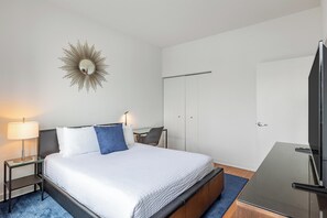 Une chambre d’hôtel avec un lit, un bureau, une chaise, une télévision, une armoire et un miroir au mur.