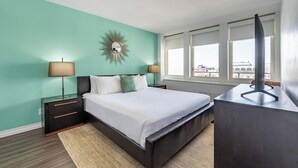 A bedroom with a bed, bedside tables, a mirror, and a view of the city through large windows. - Stylish One Bedroom Apartment in Back Bay (Boston)
