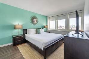 A bedroom with a bed, bedside tables, a mirror, and a view of the city through large windows. - Stylish One Bedroom Apartment in Back Bay (Boston)
