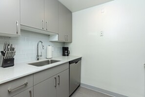 A modern kitchen with grey cabinets, a stainless steel sink, and a coffee maker. - One Bedroom Apartment in Back Bay Building (Boston)