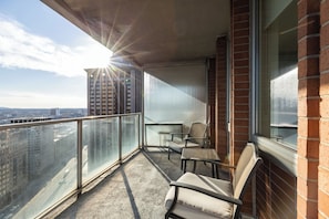 Un balcon doté d’une balustrade en verre, de deux chaises et offrant une vue sur le paysage urbain.