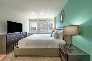 A modern bedroom with a large bed, a flat-screen TV, and a city view through the windows.