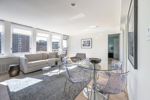 A modern living room with a glass dining table, clear chairs, a sofa, and a coffee table. - One Bedroom Apartment W/ Luxury Amenities (Boston)