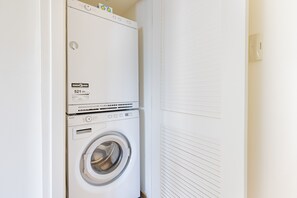 A stacked washer and dryer unit in a room with white walls and a closed door. - Modern 1 Bed Apartment in Central Back Bay, Boston (Boston)