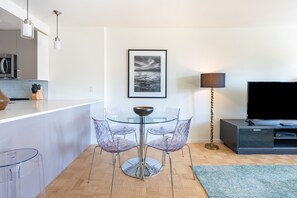 Uma cozinha moderna com micro-ondas, uma mesa de jantar de vidro com cadeiras, um quadro na parede, um abajur e uma TV em um armário.