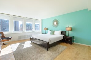 Quarto moderno com uma cama grande, duas mesas de cabeceira, uma cadeira e vista para a cidade através de grandes janelas.
