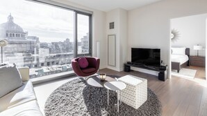 Ett modernt vardagsrum med en stor TV, bekväma sittplatser och utsikt över stadsbilden.