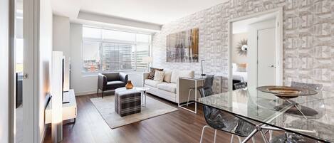 A modern living room with a glass dining table, a sofa, and a city view through large windows.