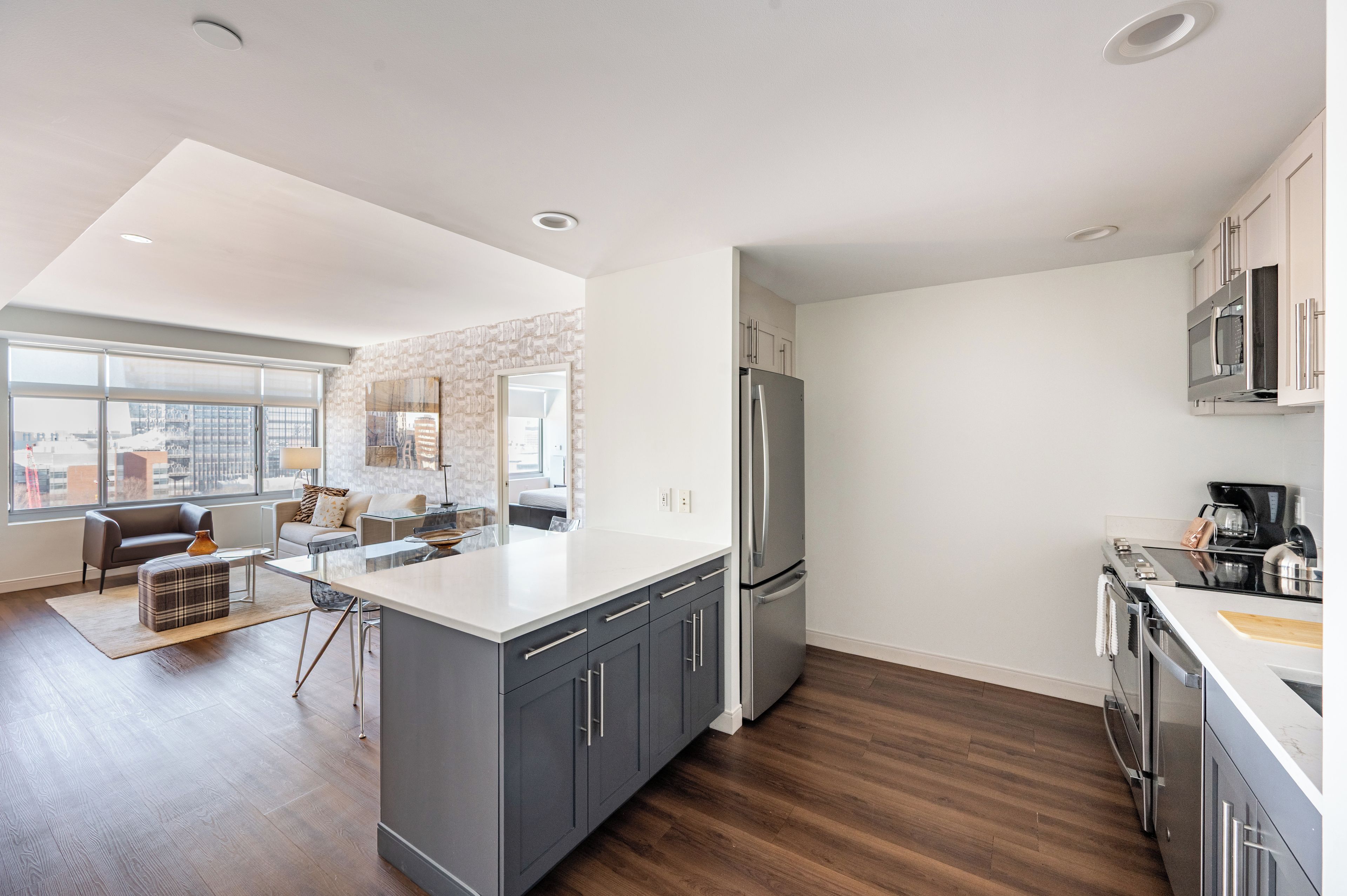 A modern kitchen with a large island, stainless steel appliances, and a city view through large windows.