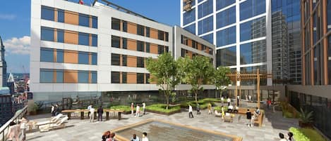 En modern byggnad med flera våningar, utomhusområden med sittplatser och en central innergård med en fontän.
