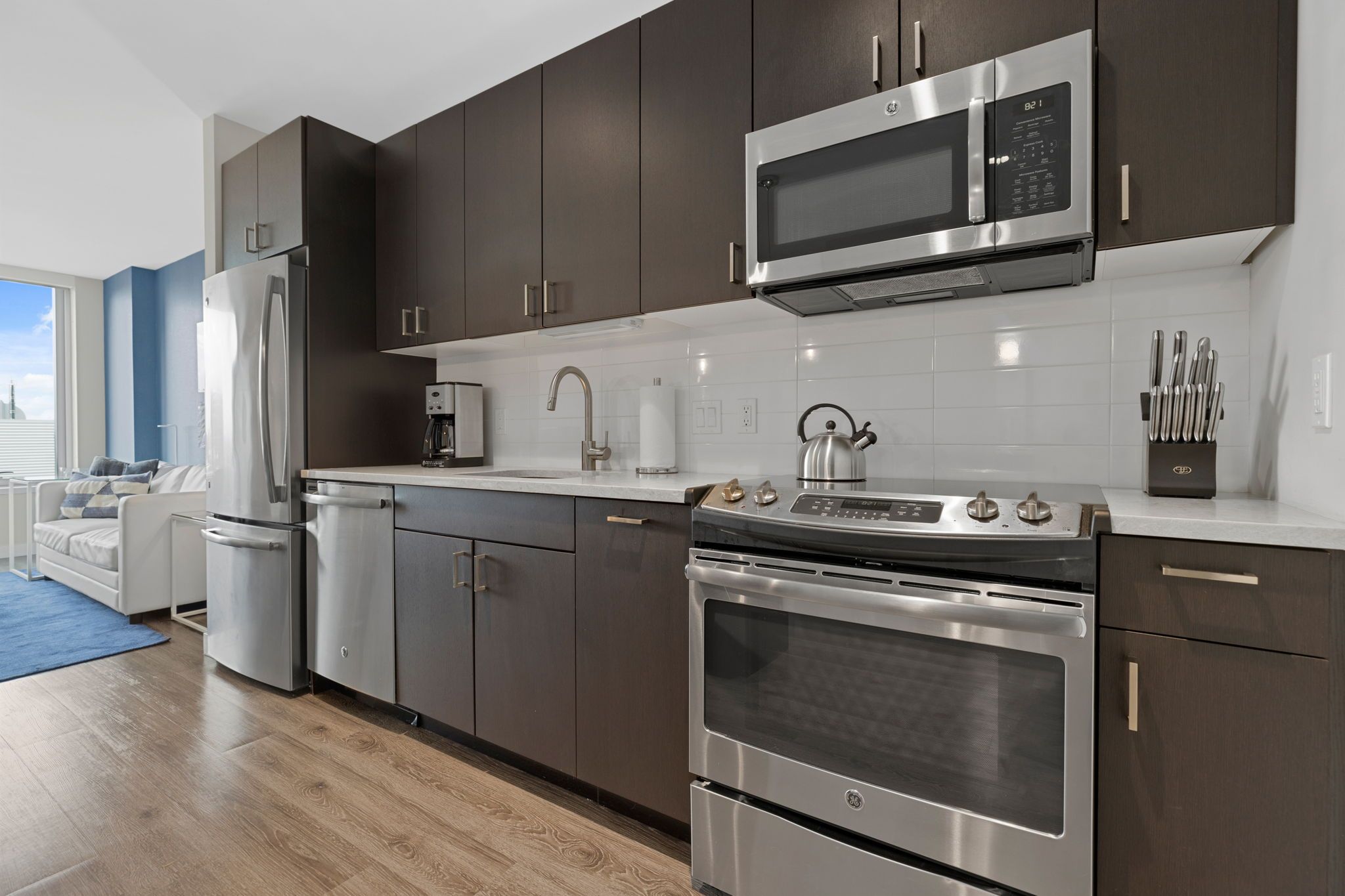 A modern kitchen with stainless steel appliances, dark cabinetry, and a white countertop.