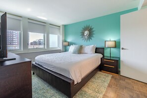 A bedroom with a bed, bedside tables, a TV, and a city view.