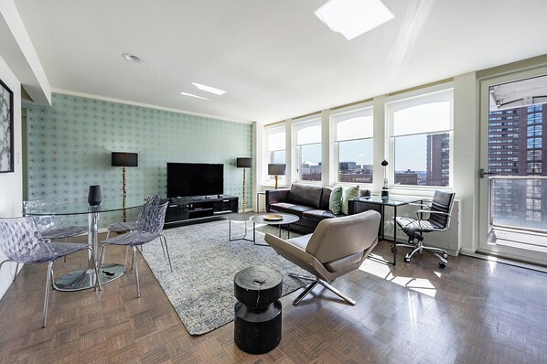A modern living room with a large TV, seating, and a city view.