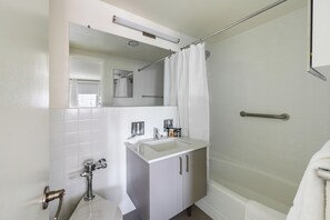 A bathroom with a sink, mirror, shower, and a towel rack.