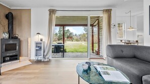 A modern living room with a fireplace, a glass coffee table, a sofa, and a view of a garden through a sliding glass door. - Stunning home in Eskebjerg with WiFi (Eskebjerg)