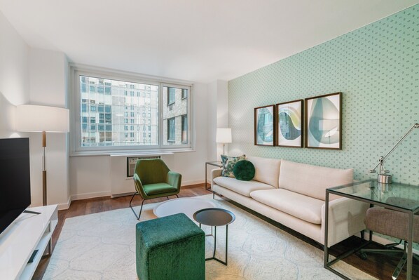 Un salon moderne avec un canapé, un fauteuil vert, une table basse en verre et un téléviseur.