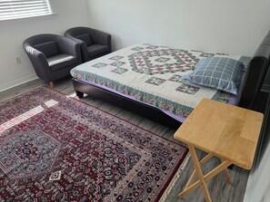 Un dormitorio con una cama, dos sillones, una mesita de madera y un tapete grande con estampado.