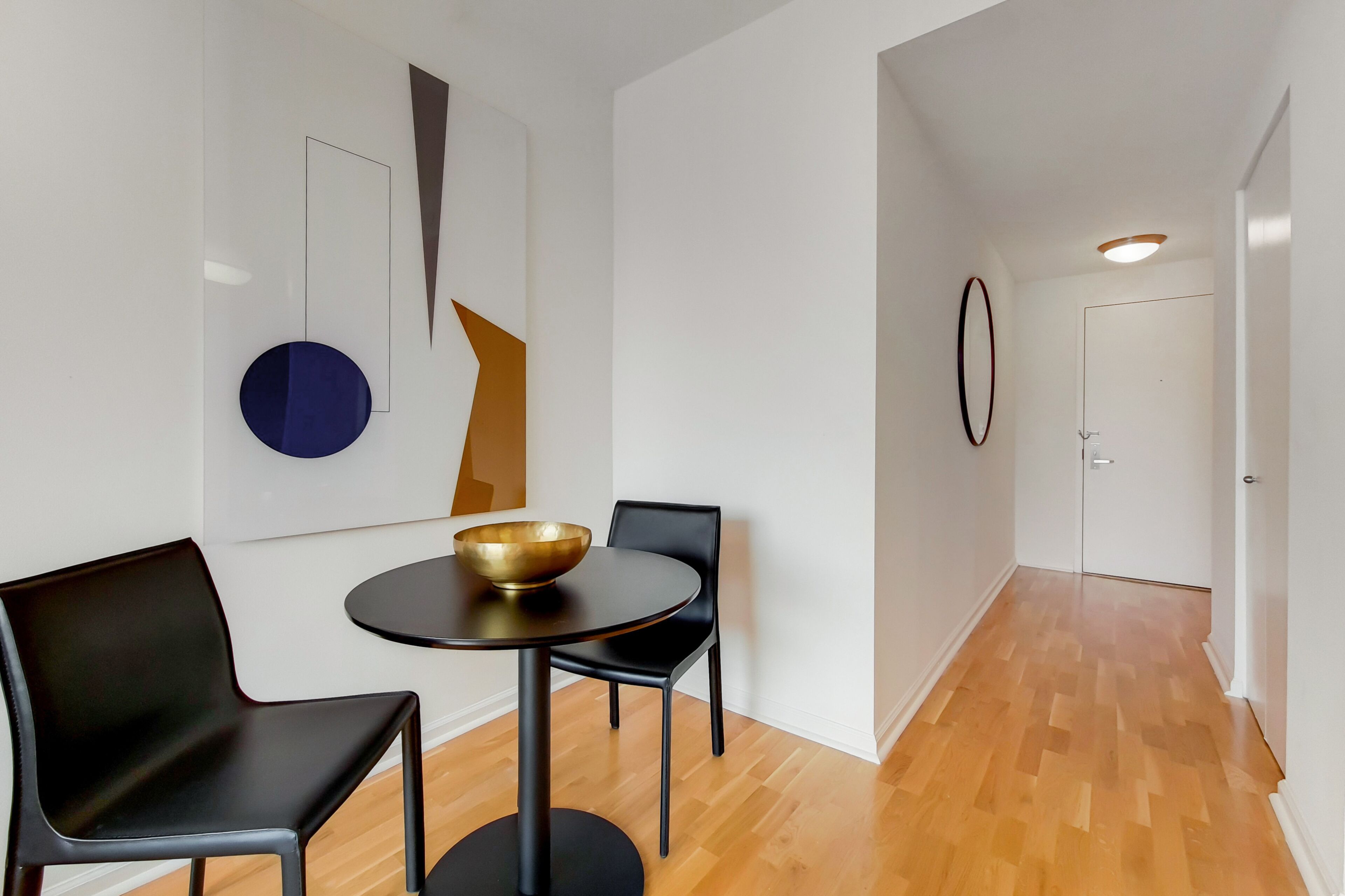 A modern interior with a round table, two black chairs, a gold bowl, and abstract wall art.