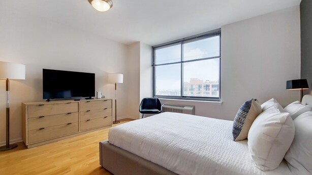 Une chambre moderne dotée d’un grand lit, d’un téléviseur à écran plat, d’un bureau et d’une fenêtre donnant sur la ville.