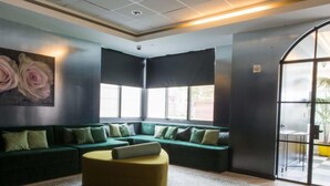 Un espace de détente moderne comprenant un canapé d’angle, un pouf rond et une grande fenêtre laissant entrer la lumière naturelle.