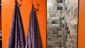 A bathroom with orange walls, two purple towels hanging on hooks, and a corner shower with tiled walls.