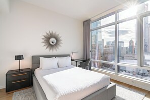 Et moderne hotelværelse med en stor seng, et skrivebord og udsigt over byen gennem store vinduer.