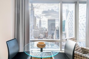 Et moderne værelse med et glasbord, to sorte stole, en stribet sofa og et stort vindue med udsigt over byens skyline.