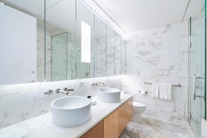 A modern bathroom with a large mirror, two sinks, a toilet, and a glass shower enclosure.