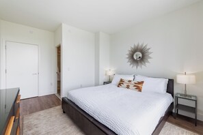 A bedroom with a large bed, two bedside tables with lamps, a mirror on the wall, and a wardrobe.