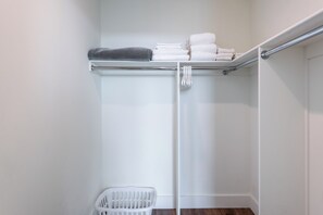 A walk-in closet with a metal rod for hanging clothes, a white plastic laundry basket, and neatly folded towels on a shelf.