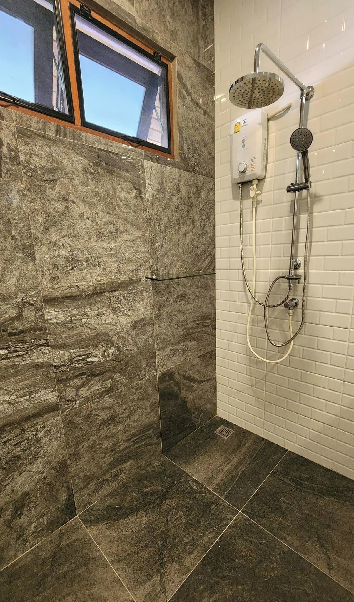 A bathroom with a stone wall, a window, and a shower with a handheld showerhead.