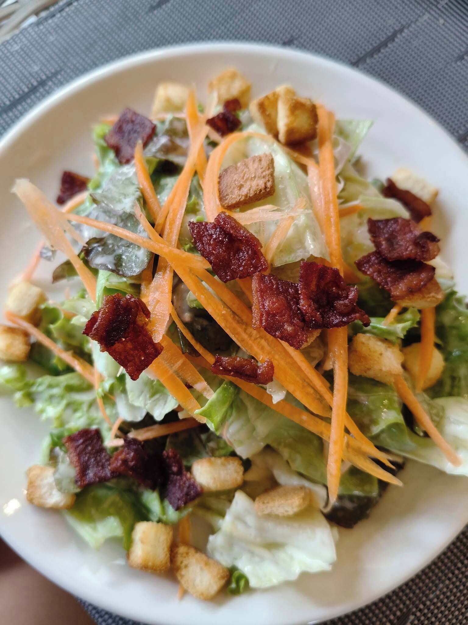 A salad with lettuce, shredded carrots, croutons, and bacon bits.