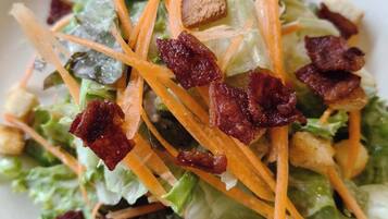 Ensalada con lechuga, zanahoria rallada, crutones y trocitos de tocino.