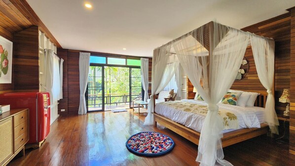 A bedroom with a four-poster bed, a red vintage refrigerator, and a large window with a view of greenery.