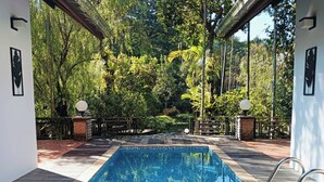 Una piscina rectangular con borde de azulejos, rodeada por una cubierta de madera y una barandilla metálica.