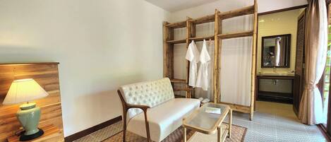 A hotel room with a sofa, a small table, a lamp, a mirror, and a wardrobe.