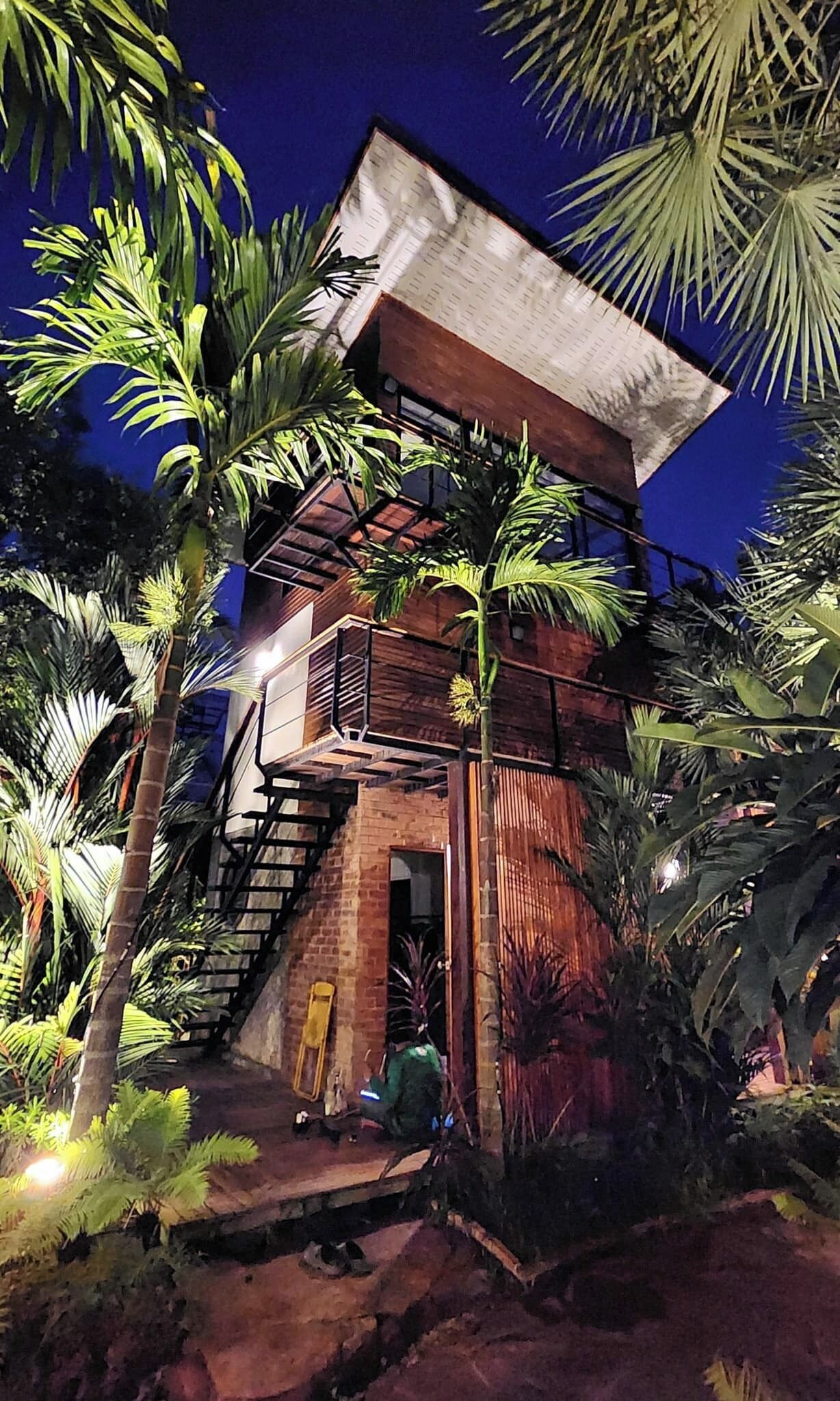 Una estructura de fusta de diversos nivells, amb una escala que condueix a un balcó superior, envoltada de vegetació tropical.