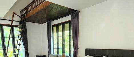 Un'ampia camera da letto con un grande letto, una scala in legno, un divano e vista sul verde dalle finestre.