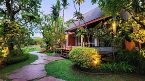 Un resort tropical con un sendero de piedra que conduce a una terraza de madera, rodeado de exuberante follaje y palmeras.