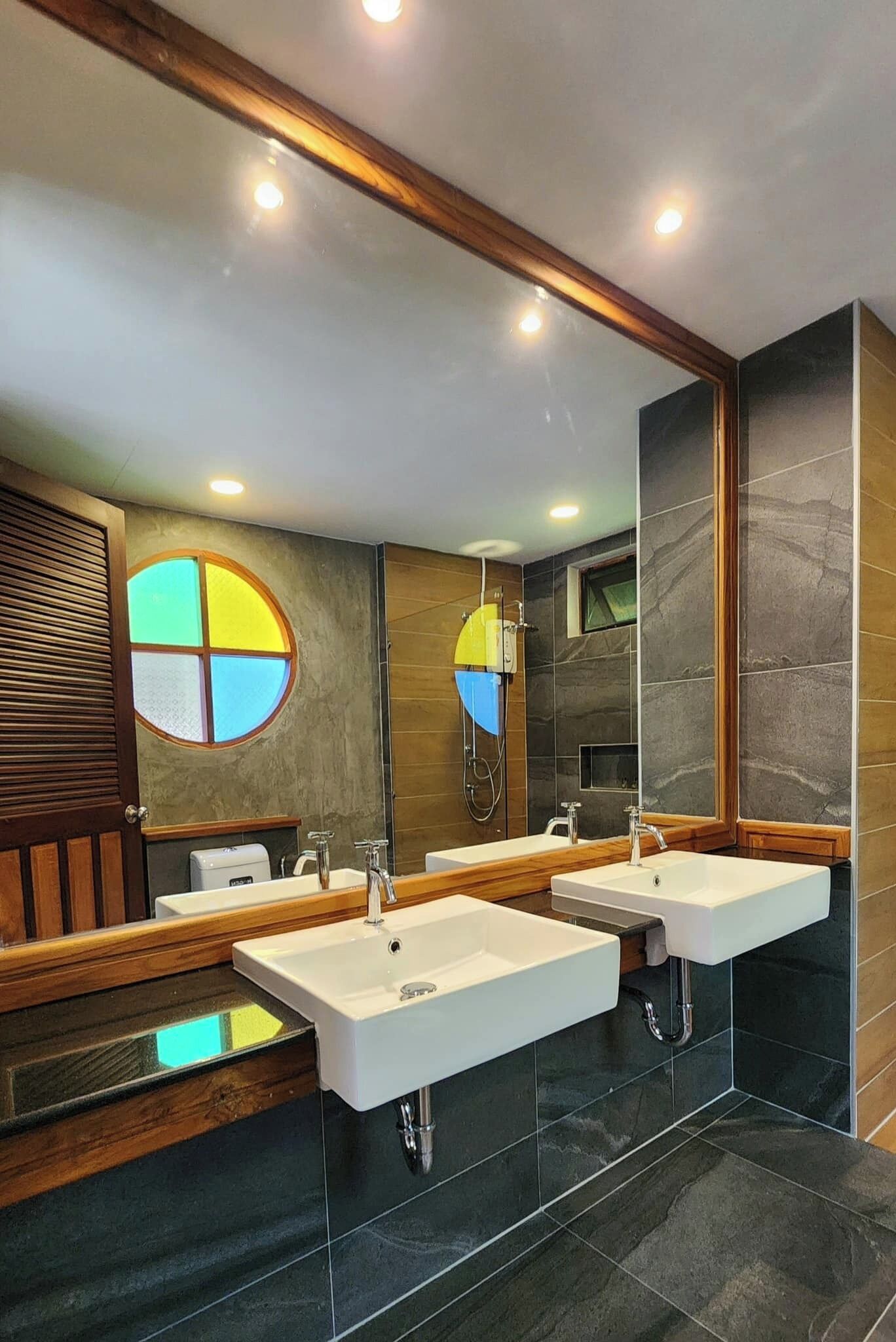 A modern bathroom with two sinks, a large mirror, and a circular window.